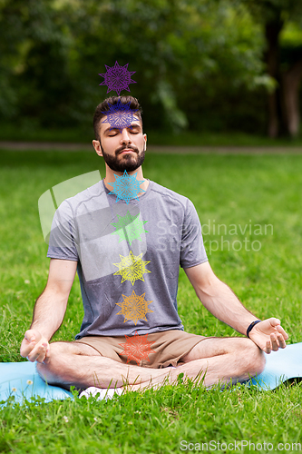 Image of young man meditating at park with seven chakras