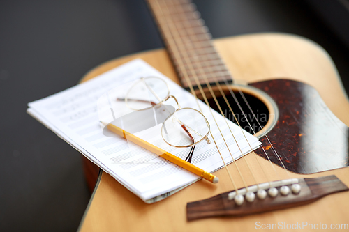 Image of close up of guitar, music book, pencil and glasses