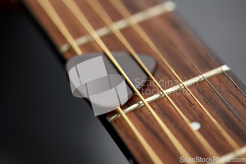 Image of close up of guitar neck with pick between strings