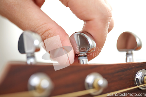 Image of close up of hand tuning guitar strings with pegs