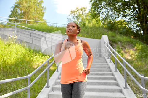 Image of african woman in earphones running outdoors