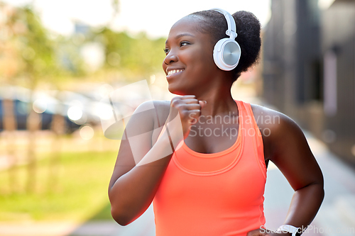 Image of happy african woman in headphones running outdoors