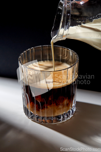 Image of hand with jug pouring cream to glass of coffee