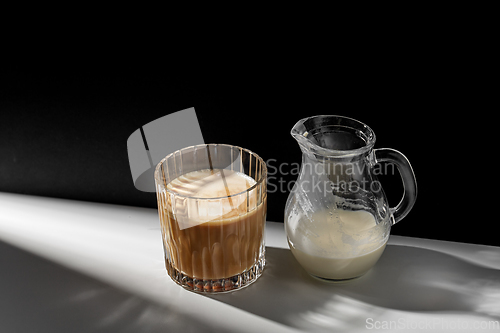 Image of coffee in glass and jug of milk or cream on table