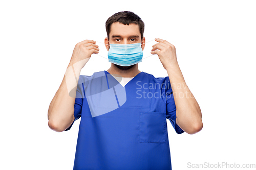 Image of male doctor in blue uniform putting on mask