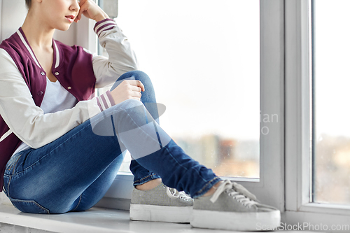 Image of sad teenage girl sitting on window sill