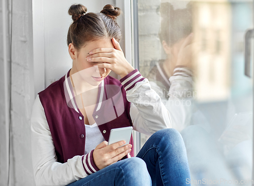 Image of teenage girl with smartphone sitting on windowsill