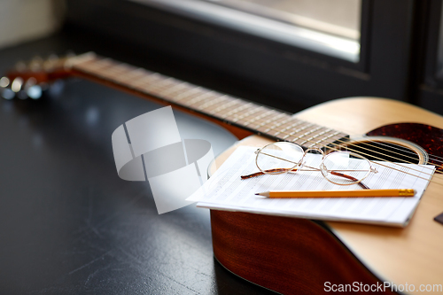 Image of close up of guitar, music book, pencil and glasses