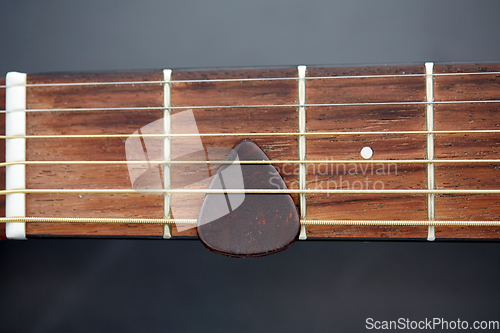 Image of close up of guitar neck with pick between strings
