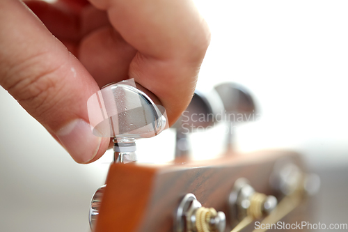 Image of close up of hand tuning guitar strings with pegs