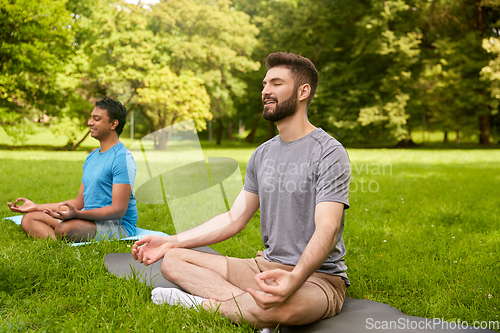 Image of men meditating in lotus pose at summer park