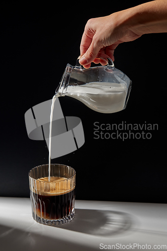 Image of hand with jug pouring cream to glass of coffee