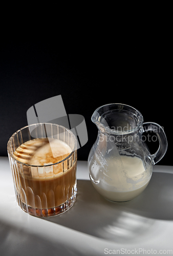 Image of coffee in glass and jug of milk or cream on table