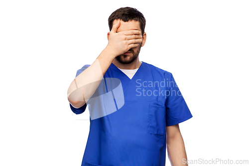 Image of tired doctor or male nurse covering eyes with hand