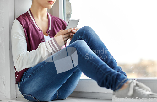 Image of teenage girl with smartphone sitting on windowsill