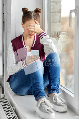 Image of teenage girl with smartphone sitting on windowsill