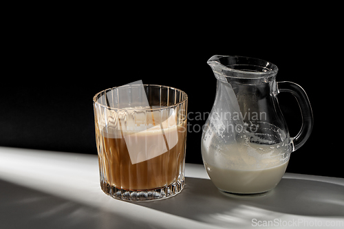 Image of coffee in glass and jug of milk or cream on table