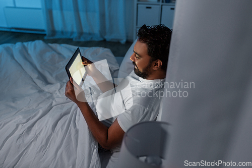 Image of indian man with tablet pc in bed at home at night