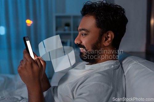 Image of indian man with smartphone in bed at home at night