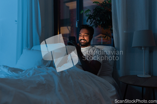 Image of indian man with smartphone in bed at home at night