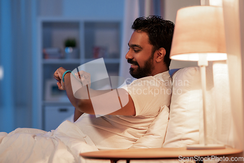 Image of indian man with health tracker in bed at night