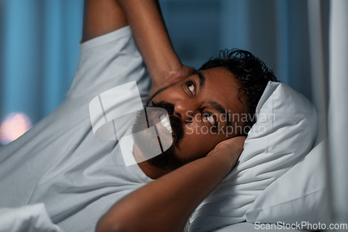 Image of annoyed indian man lying in bed and closing ears