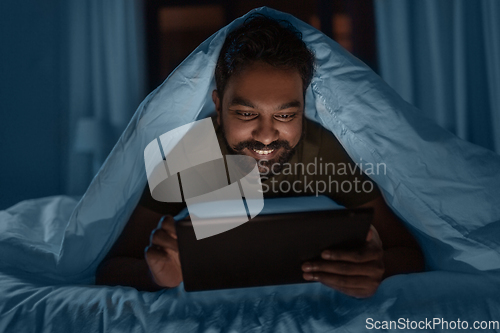 Image of indian man with tablet pc in bed at home at night