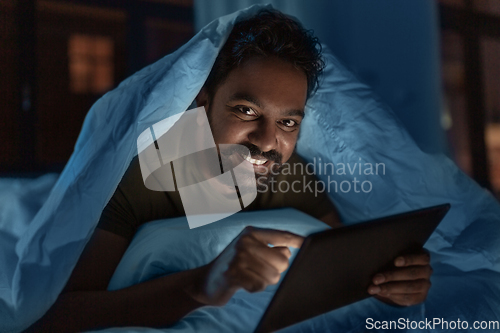 Image of indian man with tablet pc in bed at home at night