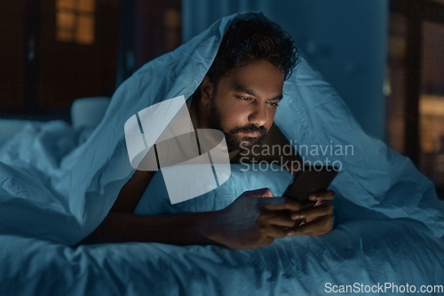 Image of indian man with smartphone in bed at home at night