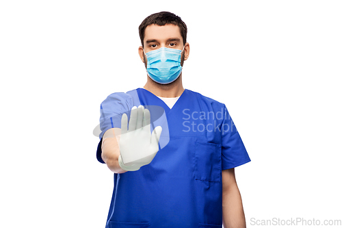 Image of male doctor in blue uniform and mask showing stop