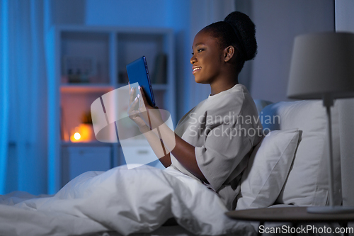 Image of woman with tablet pc in bed at home at night