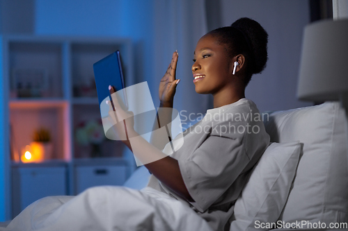 Image of woman with smartphone and earbuds in bed at night