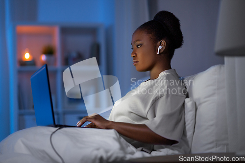 Image of woman with laptop and earphones in bed at night