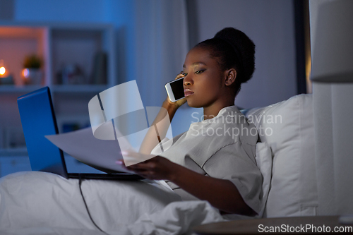 Image of woman with laptop calling on smartphone in bed