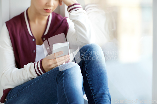 Image of teenage girl with smartphone sitting on windowsill