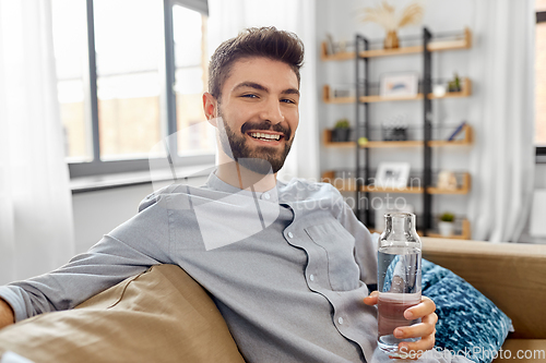 Image of happy man drinking water from glass bottle at home