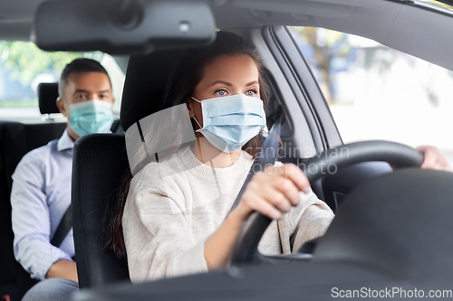 Image of female driver in mask driving car with passenger