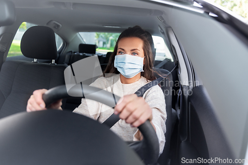 Image of woman or female driver in mask driving car in city