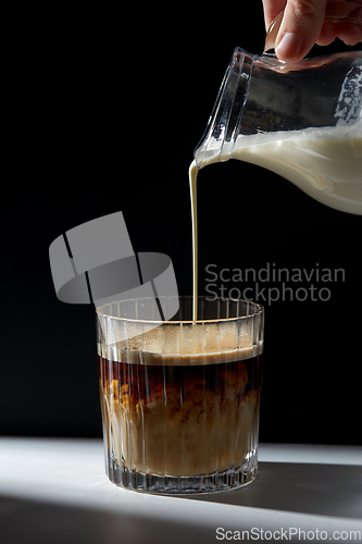Image of hand with jug pouring cream to glass of coffee