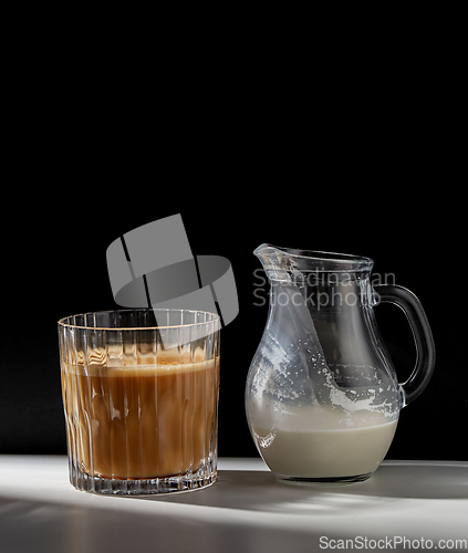 Image of coffee in glass and jug of milk or cream on table