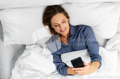 Image of young woman with smartphone lying in bed