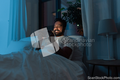 Image of indian man with smartphone in bed at home at night