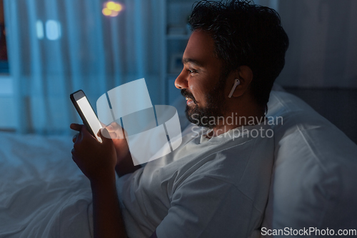 Image of man with smartphone and earphones in bed at night