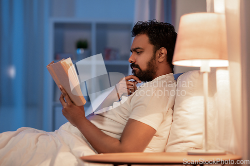 Image of indian man reading book in bed at night