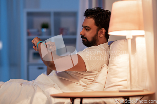 Image of indian man with health tracker in bed at night