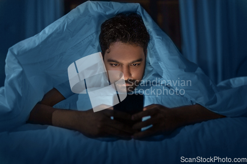 Image of indian man with smartphone in bed at home at night