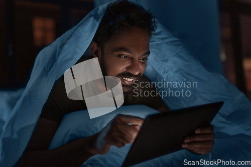 Image of indian man with tablet pc in bed at home at night