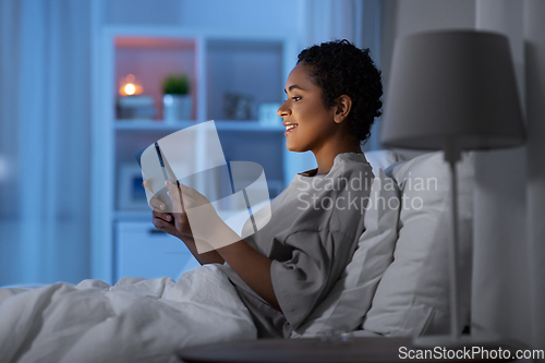 Image of woman with tablet pc in bed at home at night