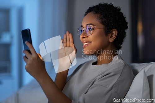 Image of woman with phone having video call in bed at night