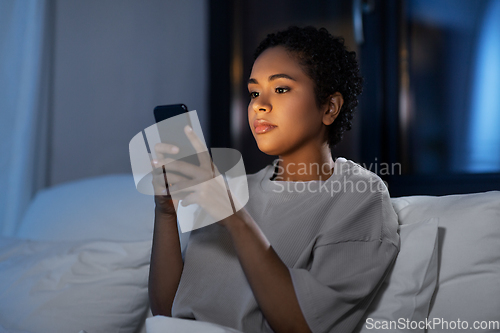 Image of african woman with smartphone in bed at night